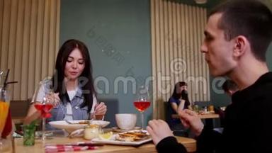 一对年轻夫妇坐在咖啡馆的桌子旁。 吃海鲜和意大利面